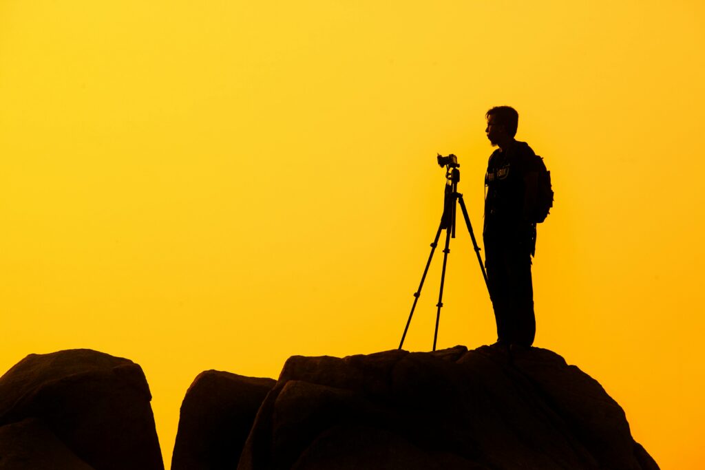 pexels-photo-22185 Silhouette of a lone photographer with tripod on a rocky cliff against a golden sunset sky.