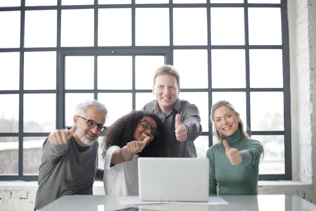 pexels-photo-3931866-3931866 Happy multiracial team sitting at table with laptop and working on successful project while demonstrating thumb up gesture and smiling at camera