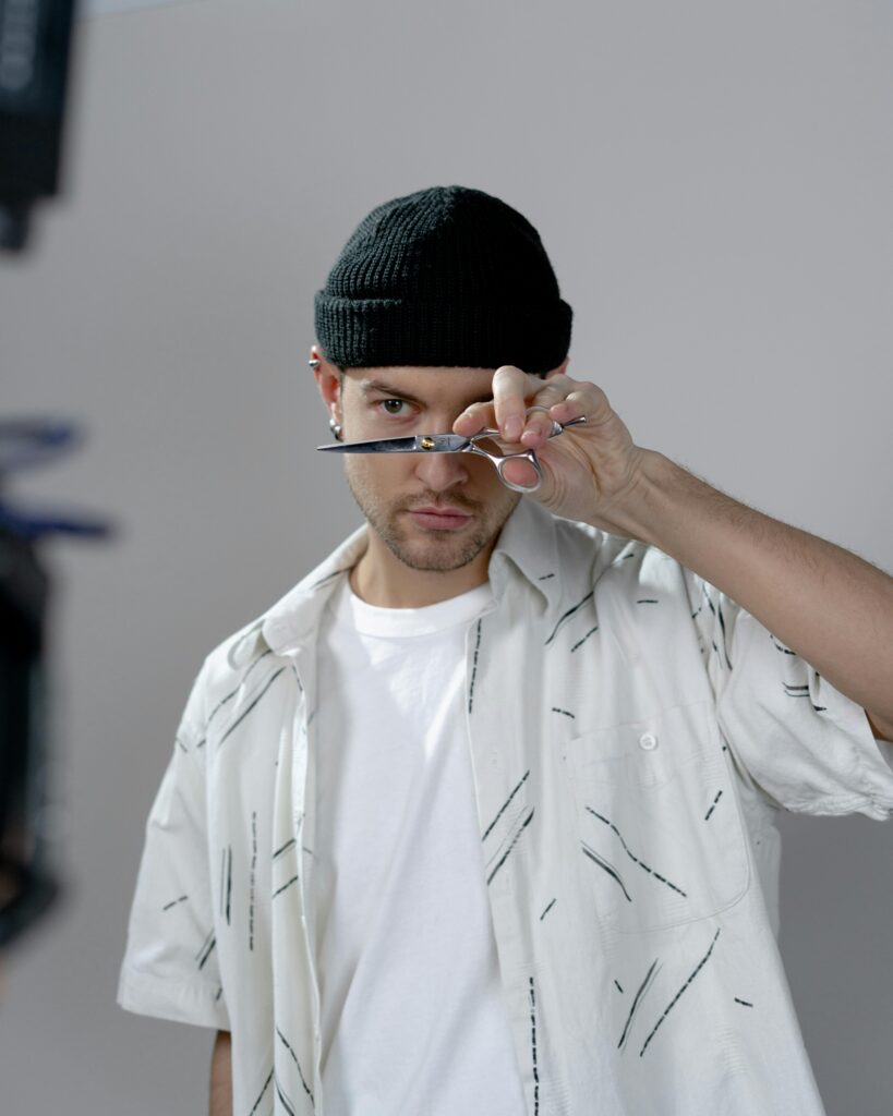 A stylish hairdresser wearing a beanie holding scissors in a modern salon setting.